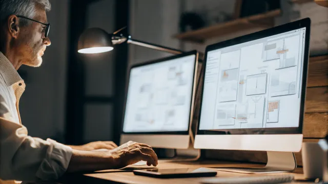 A busy engineer looking overwhelmed at their desk surrounded by stacks of code and project files